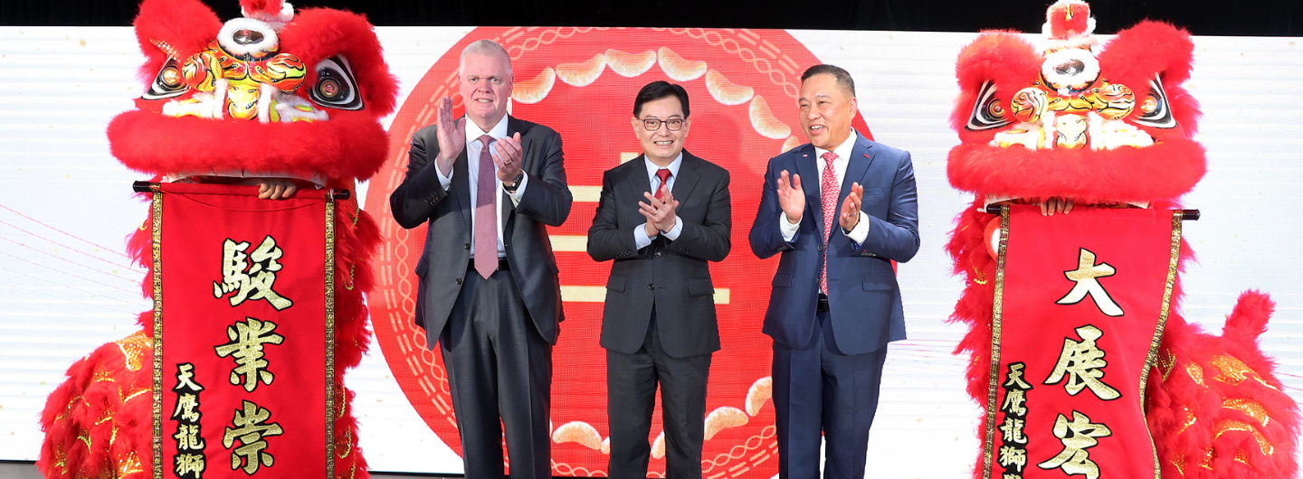 Three people in suits, flanked by Chinese lion dancers holding banners.